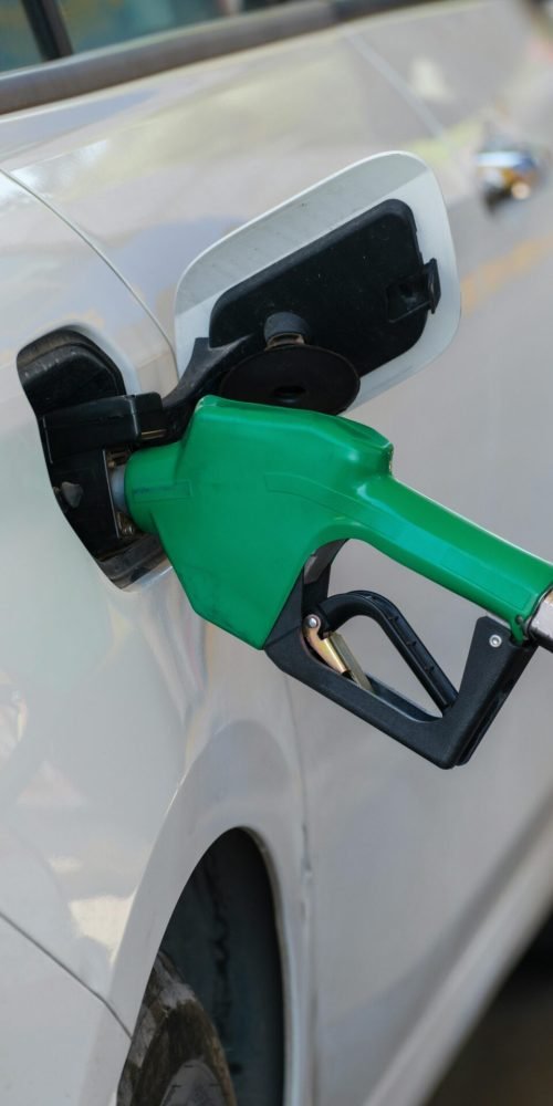 Close-up of a green nozzle refueling a white car at a gas station.